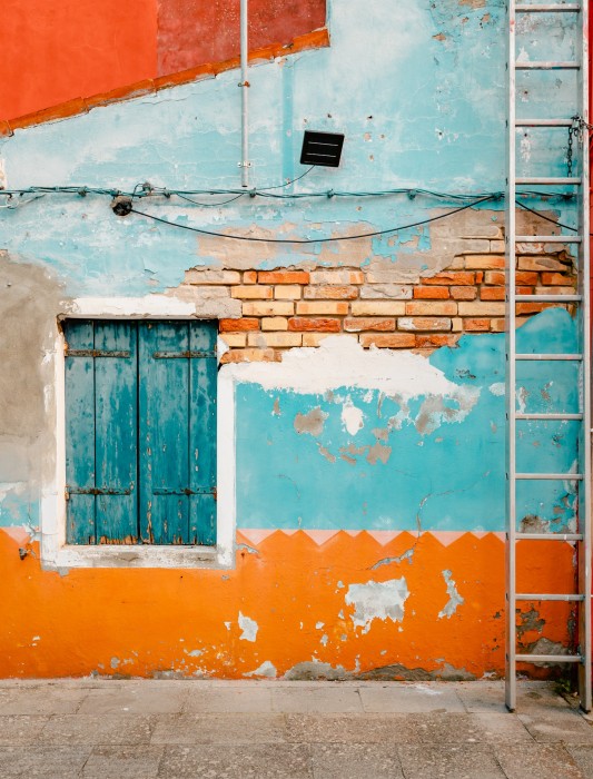 Burano, Italy - October 2022: Ancient facade of dwelling with ruined orange and blue plaster