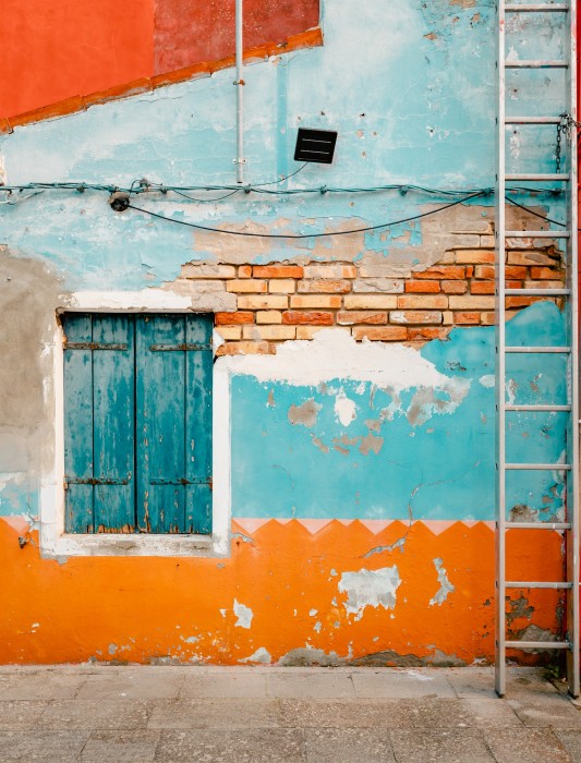 Ancient facade of dwelling with ruined orange and blue plaster Burano, Italy - October 2022: Ancient facade of dwelling with ruined orange and blue plaster